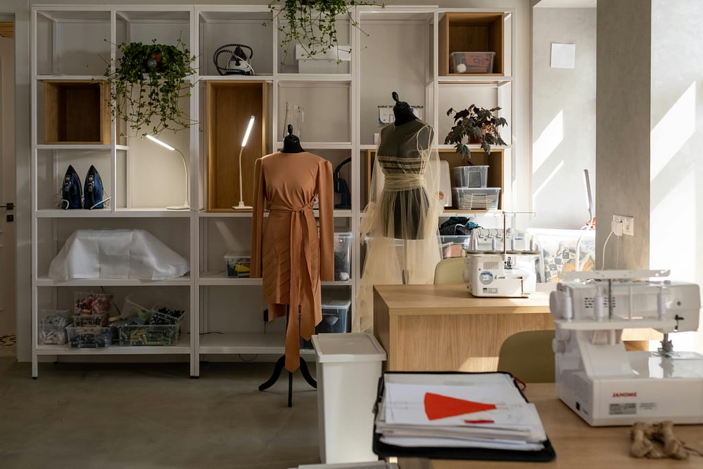 A fashion studio with mannequins, sewing machines, and organized shelves, bathed in natural sunlight.