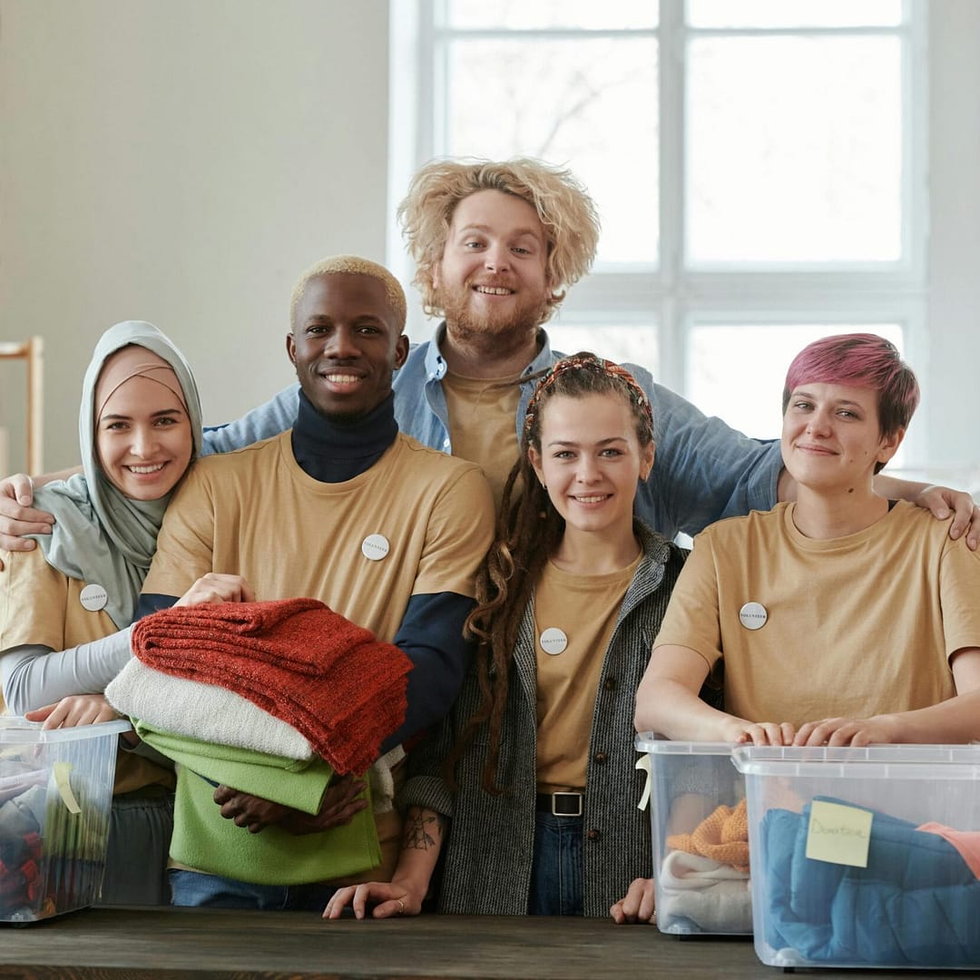 Group of diverse volunteers smiling while sorting clothes at a charity donation center.