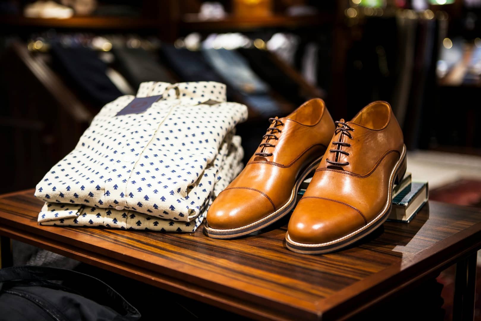 Elegant brown leather shoes and printed shirt displayed on a wooden table in a stylish clothing store.