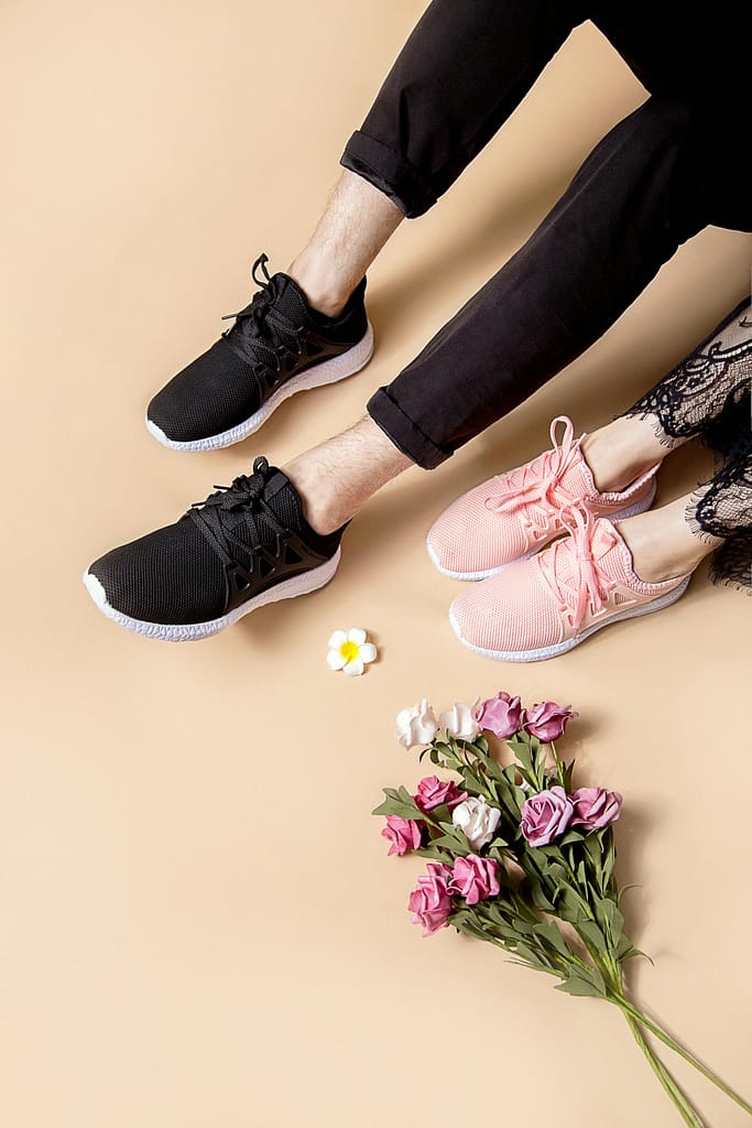 Pair of black and pink sneakers beside a bouquet of colorful flowers on a neutral background.