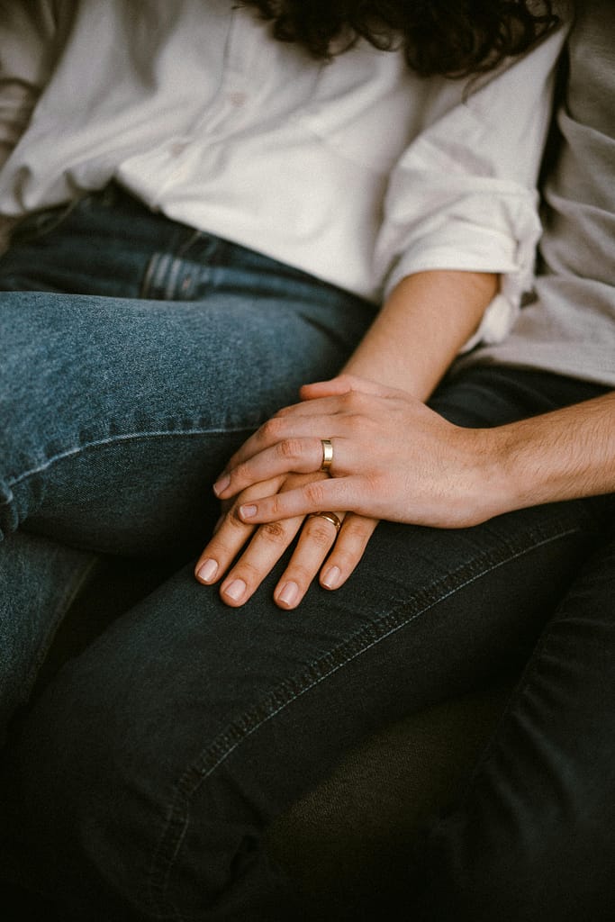 Hands Wearing Wedding Rings Resting on Mans Lap