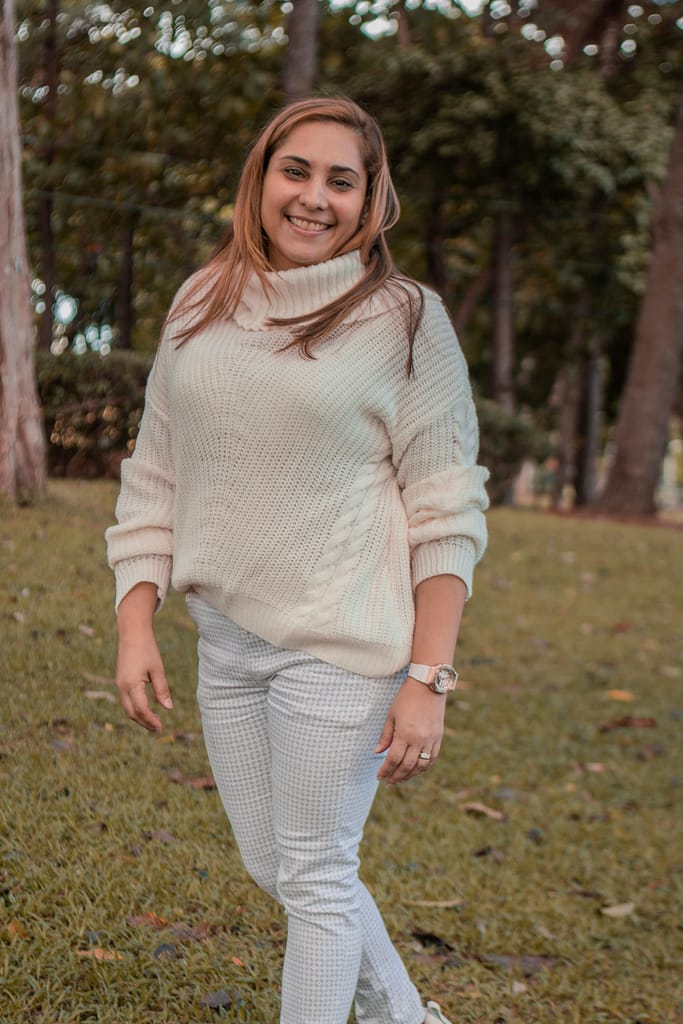 Woman in a warm sweater smiling while standing in a park setting during the day.