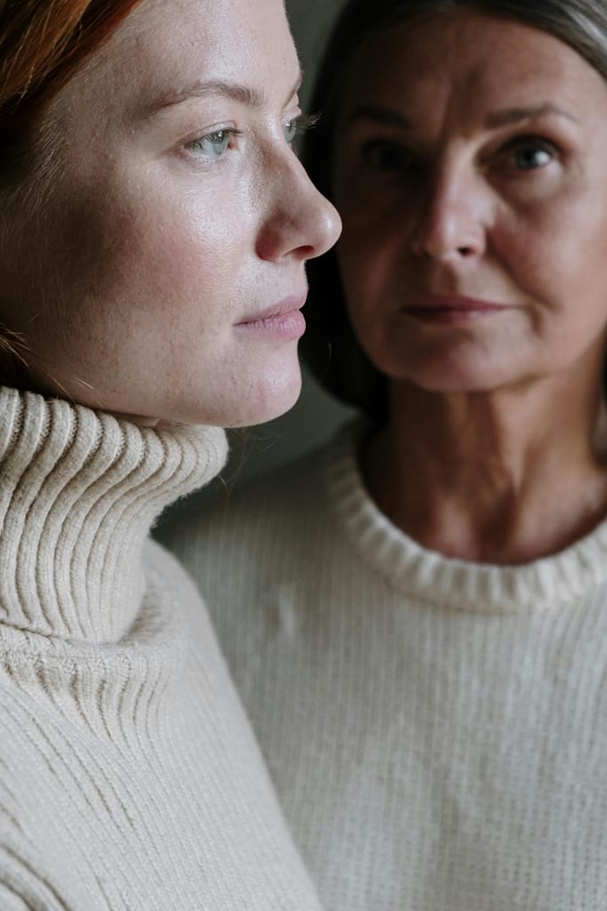 Close-up portrait of two women wearing knitted sweaters. Intimate and serene setting.