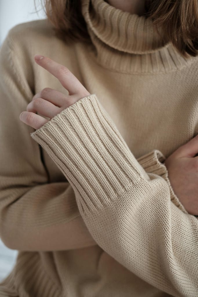 Detailed view of a beige knitted sweater with ribbed cuffs and turtleneck indoors.