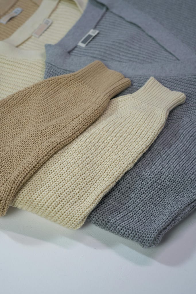 A collection of folded knit sweaters in earthy tones displayed in a flat lay arrangement.